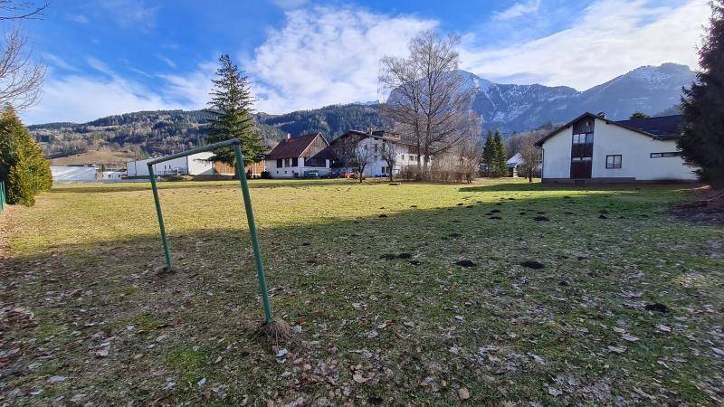 Weitläufige Wiese mit Blick auf die umliegende Berglandschaft und traditionelle Häuser.