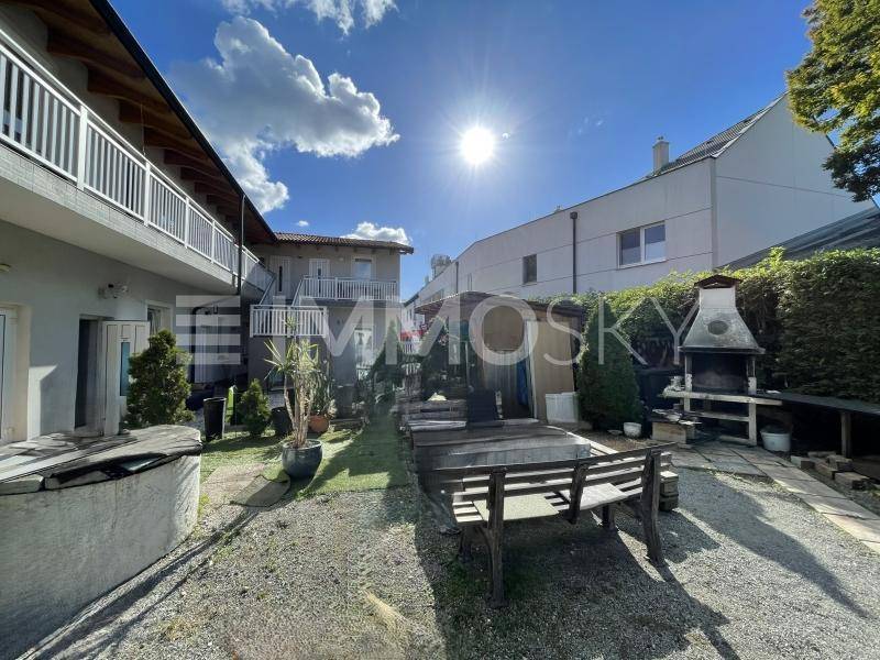 Heller Außenbereich mit Grillplatz, Holzbänken und Blick auf die Gebäudefassade.