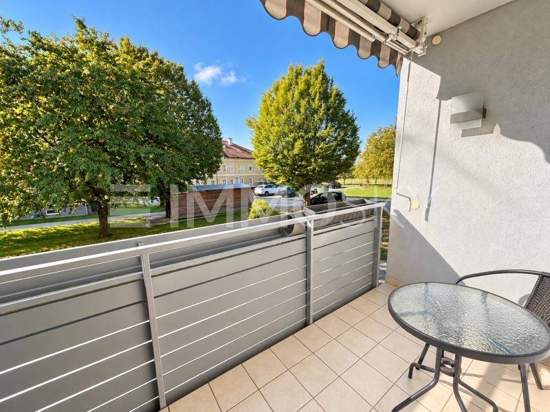 Sonniger Balkon mit kleinem Tisch und Stühlen, umgeben von Bäumen und mit Blick auf die Umgebung.