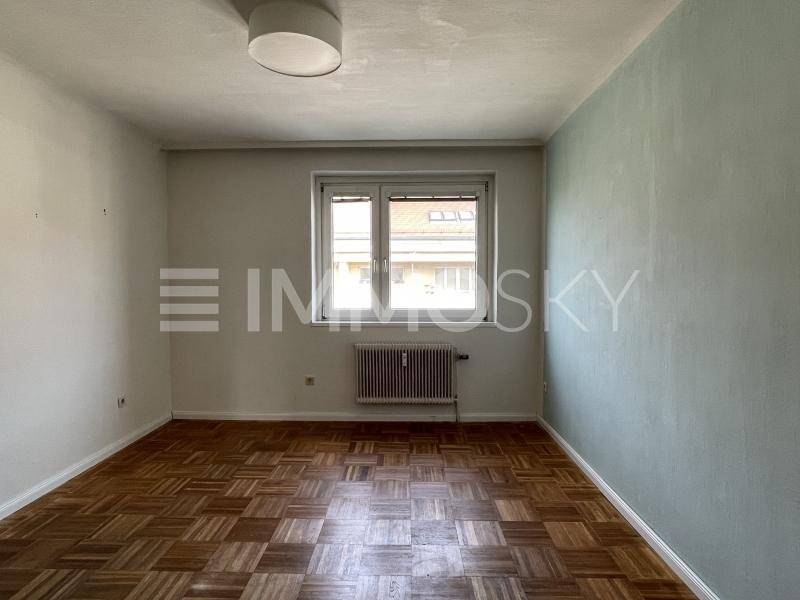 Leeres Zimmer mit klassischem Parkettboden, Heizkörper und Fenster.