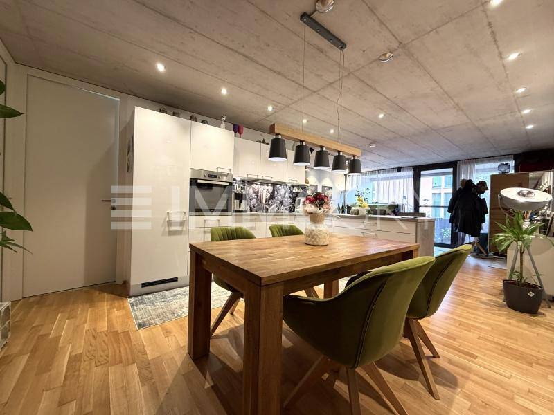 Moderne offene Küche mit Essbereich, weißen Schränken, Holzboden und Betondecke.