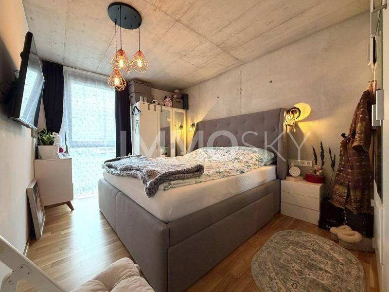 Gemütliches Schlafzimmer mit großem Bett, Holzboden, Betondecke und viel Tageslicht.