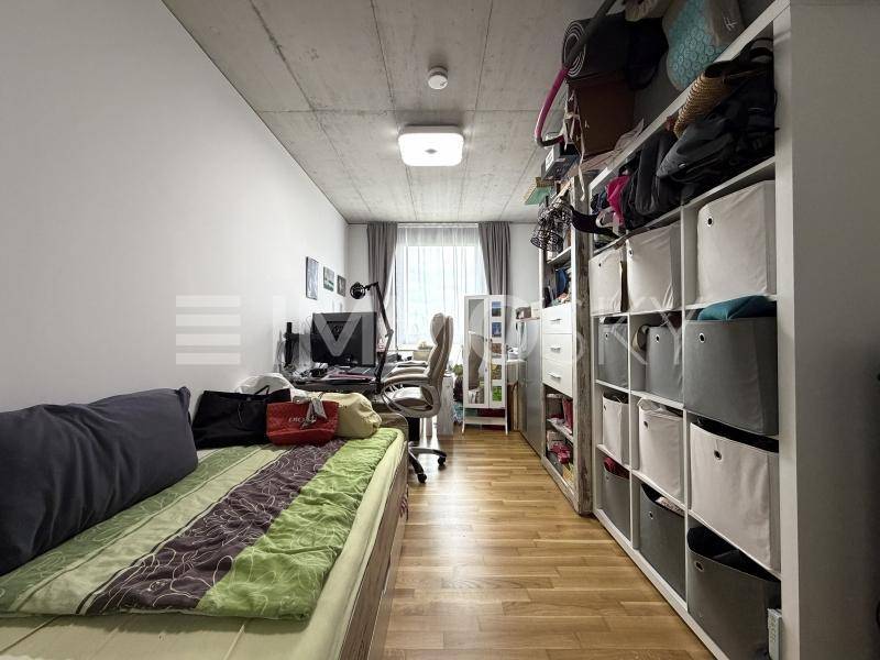 Funktionaler Arbeitsbereich mit Schreibtisch, Regalwand, Einzelbett und Holzboden.