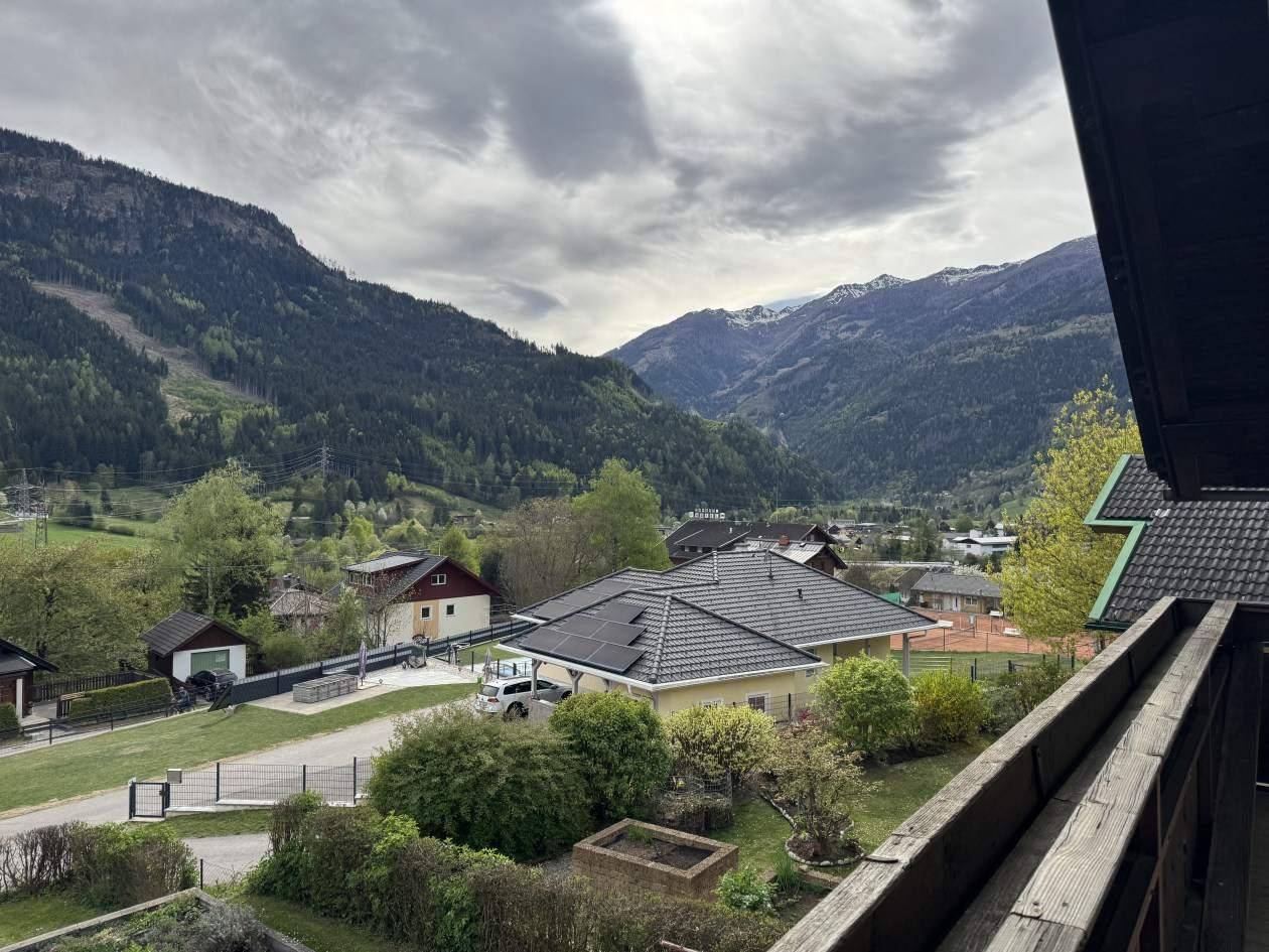 Weitläufiger Blick von einem Balkon auf die umliegende Berglandschaft und ein Dorf mit Solaranlagen.