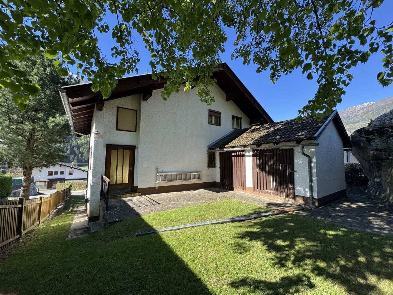Seitenansicht des Hauses mit integrierter Garage, kleiner Rasenfläche und Zugang zum Gartenbereich.
