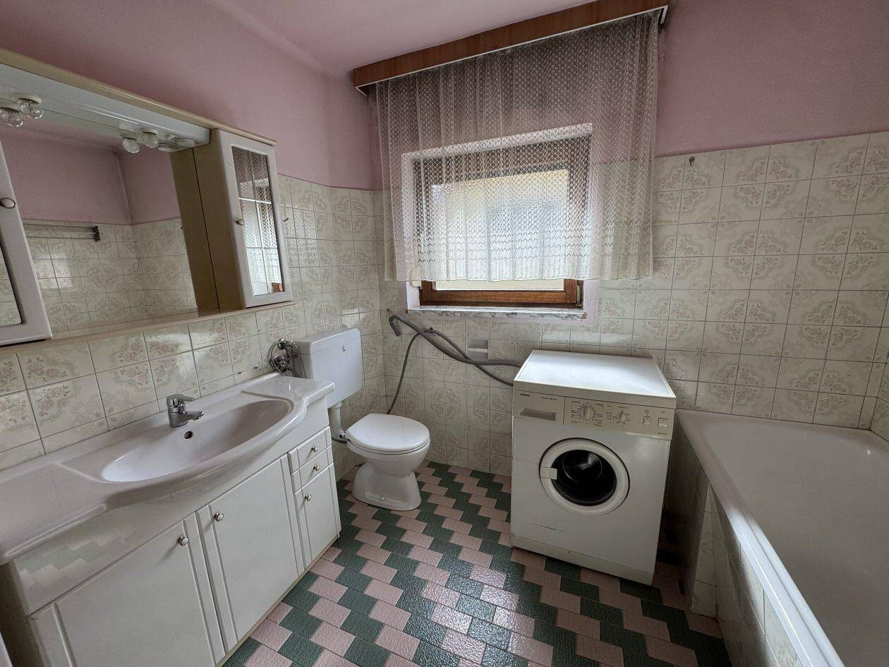 Badezimmer im 80er-Jahre-Stil mit Badewanne, Waschbecken, farbigen Fliesen und Fenster.