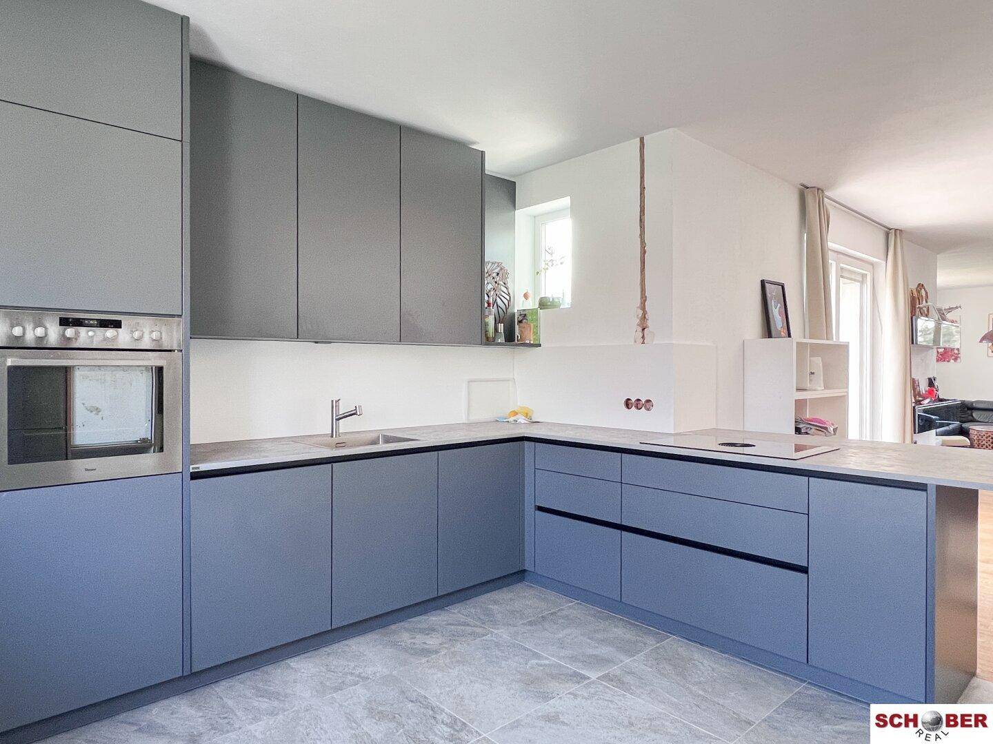 Moderne Küche mit grauen und blauen Schränken, integriertem Backofen und Fliesenboden.