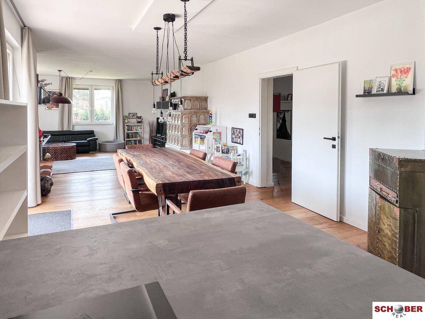 Offener Wohn-Essbereich mit großem Holztisch, Parkettboden und Blick in den Wohnbereich.