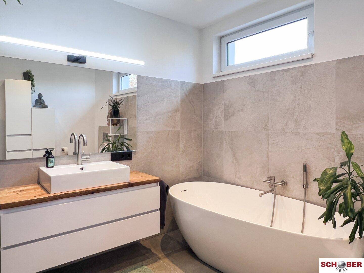 Elegantes Badezimmer mit freistehender Badewanne, großem Waschtisch und Fenster für Tageslicht.