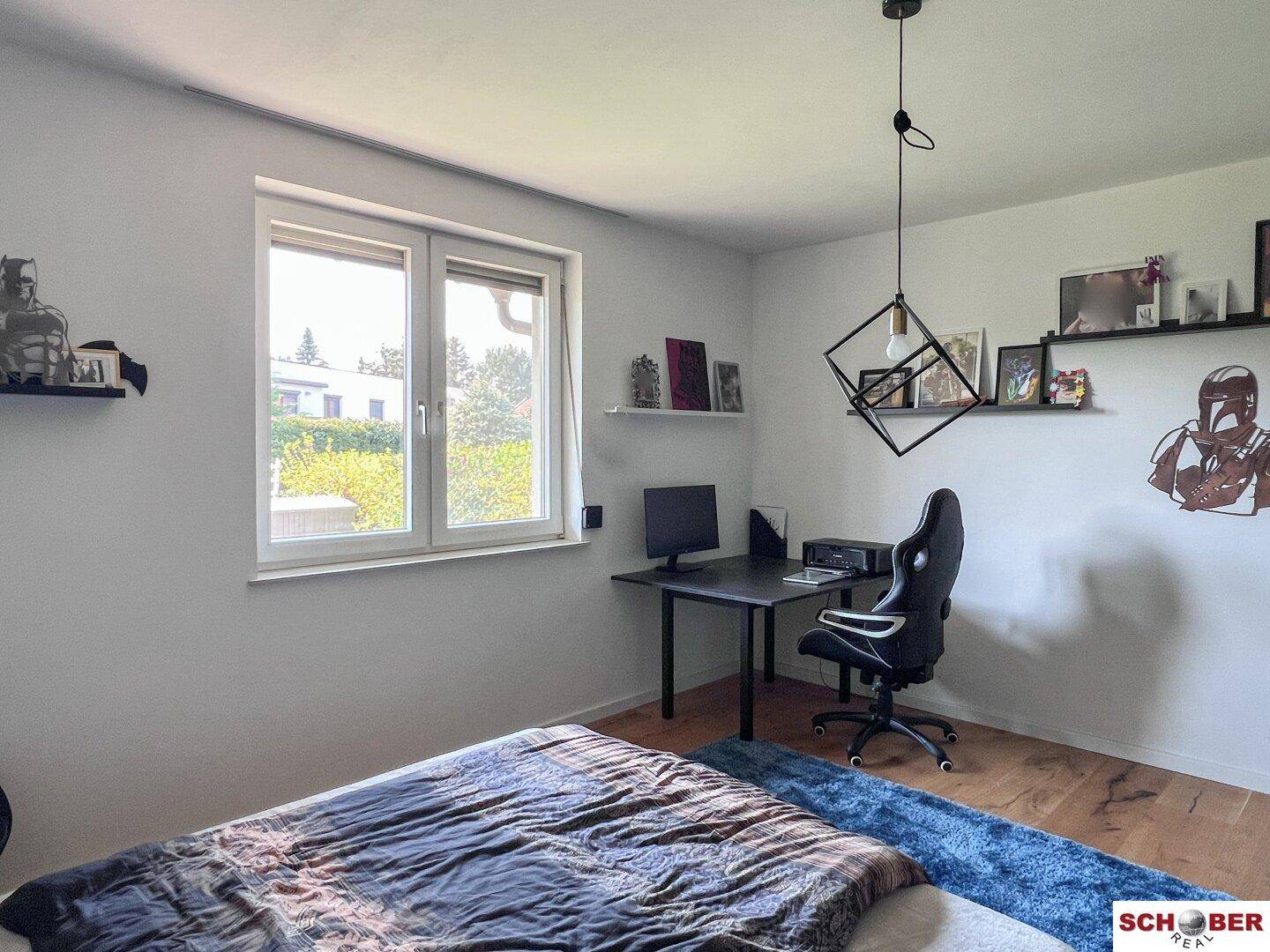 Schlafzimmer mit Holzboden, großem Fenster und modernem Schreibtischbereich.