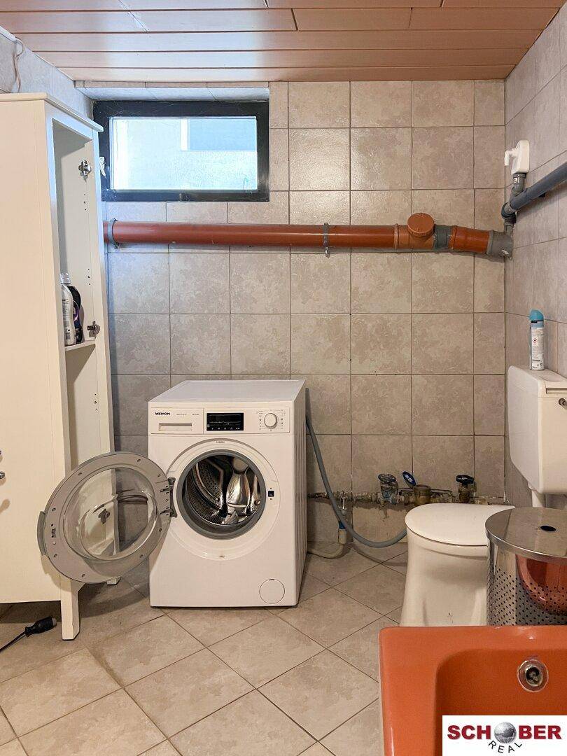 Waschküche im Keller mit Waschmaschine, WC und Fenster.