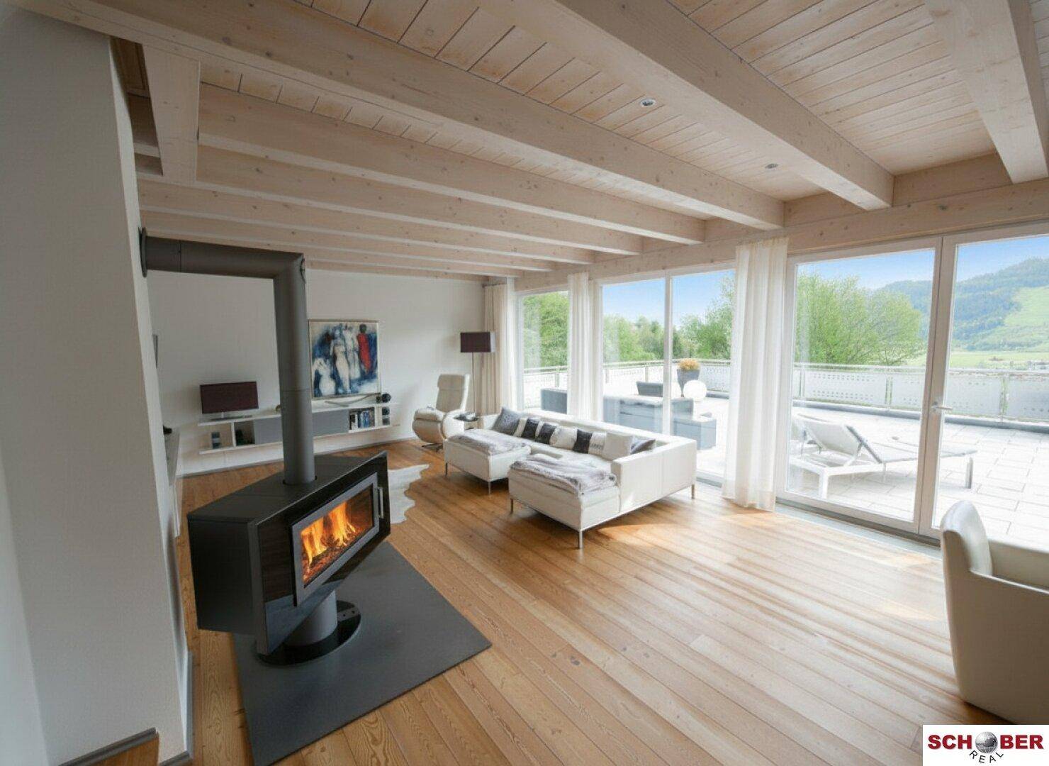 Helles Wohnzimmer mit Holzbalkendecke, Kaminofen und Zugang zur Terrasse.