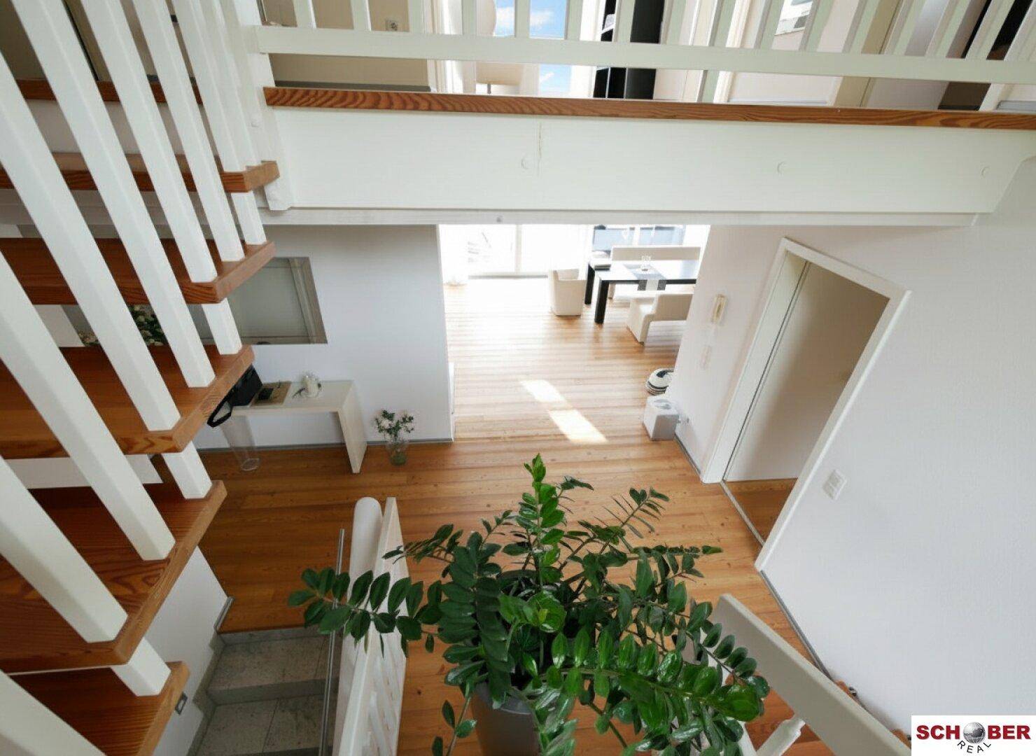 Blick von der Holztreppe in den offenen Wohnbereich mit viel Tageslicht.