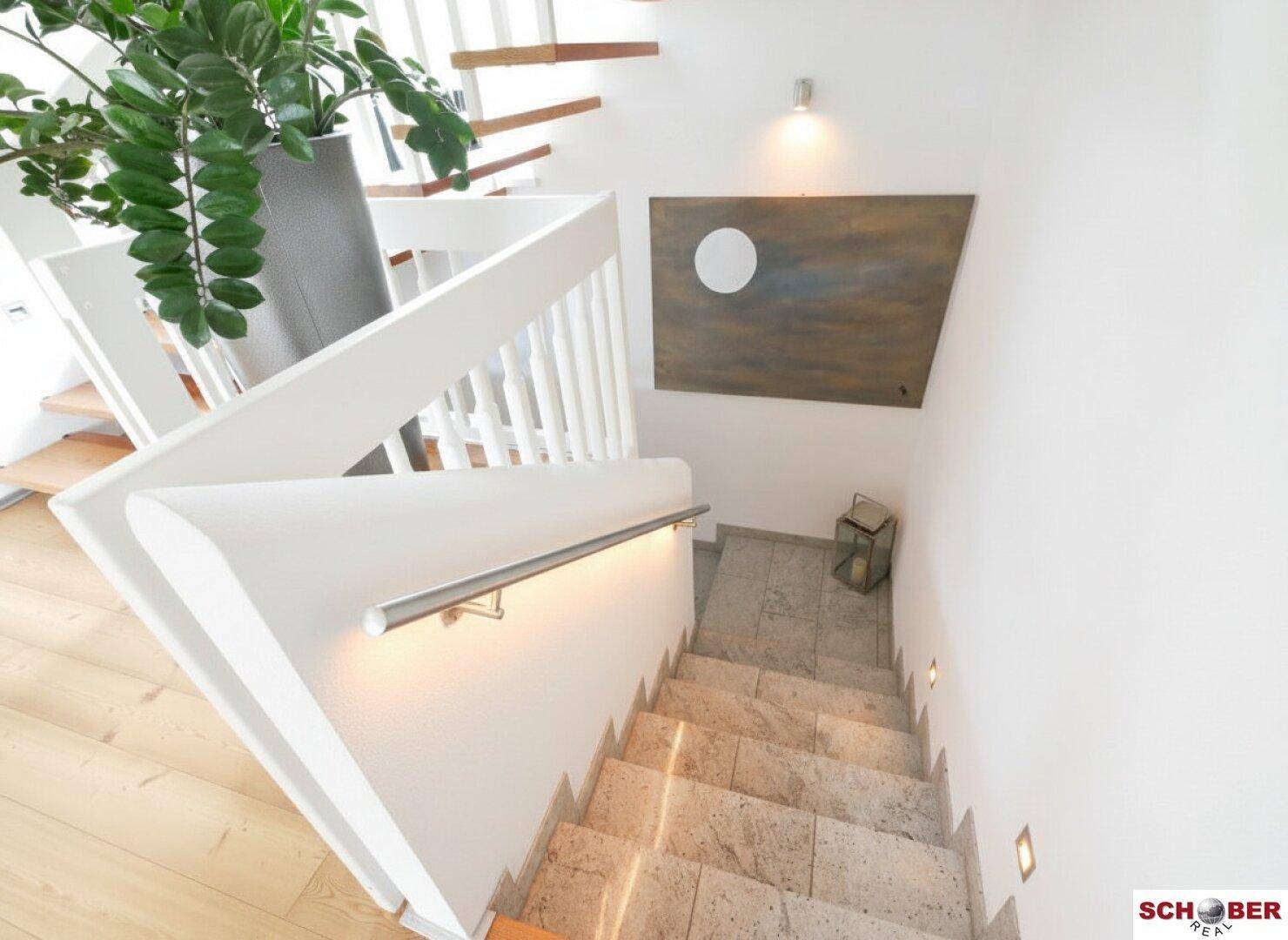 Elegante Treppe mit Steinboden und indirekter Beleuchtung, die in den unteren Bereich führt.