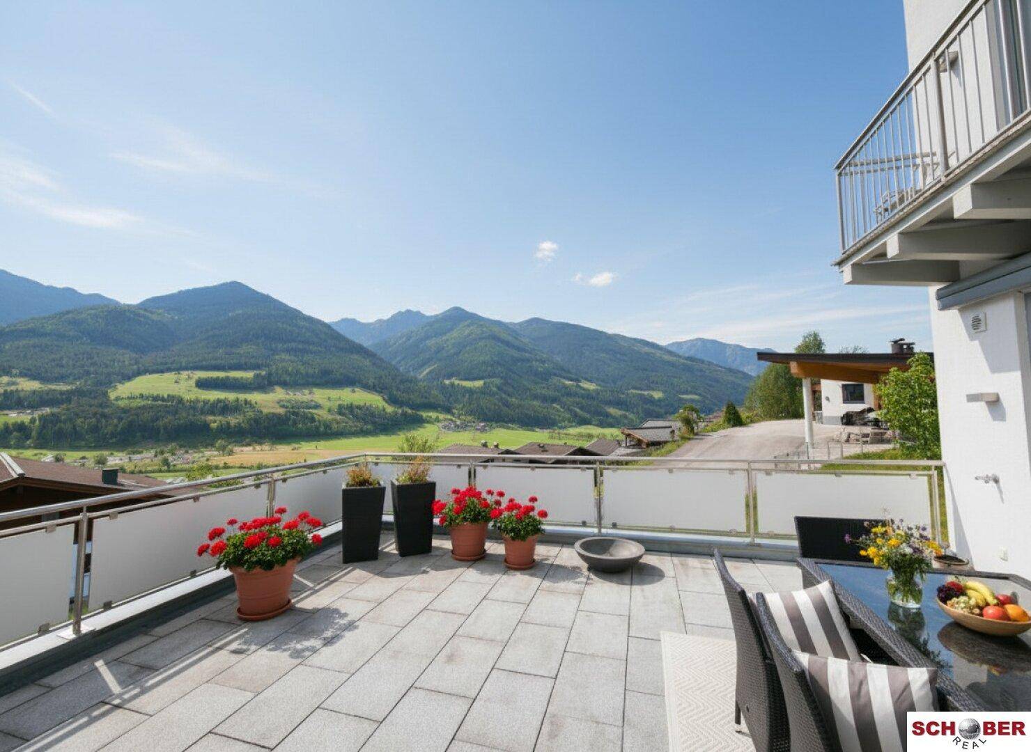 Gemütliche Terrasse mit Blumen und Essbereich, umgeben von Berglandschaft.