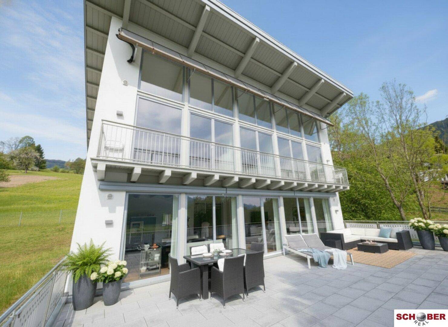 Modernes Haus mit großer Terrasse, Glasfronten und Bergblick.