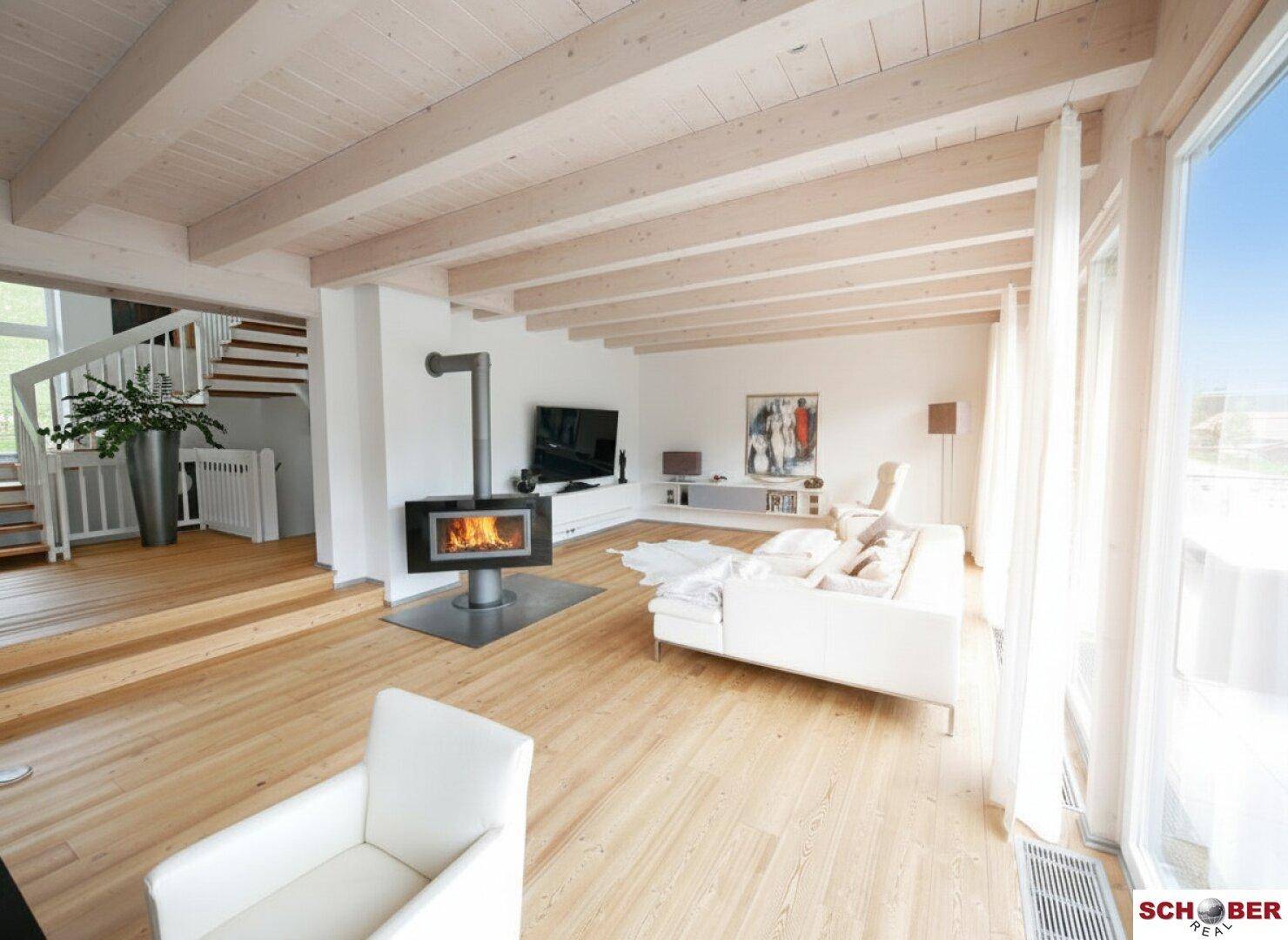 Geräumiges Wohnzimmer mit Kaminofen, Holzbalkendecke und viel Tageslicht.
