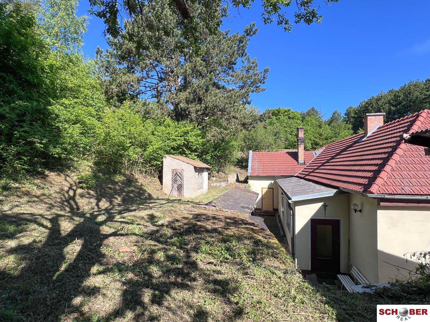Seitenansicht des Hauses mit einem kleinen Schuppen und viel Grün in sonniger Umgebung.