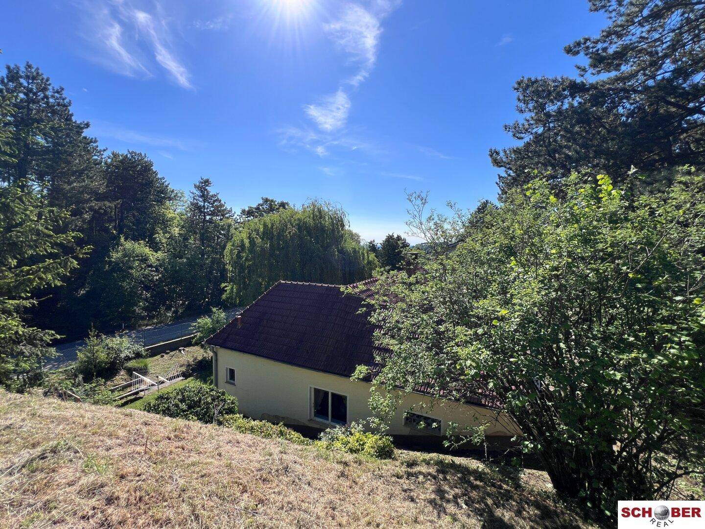Haus eingebettet in eine grüne Hügellandschaft unter strahlend blauem Himmel.