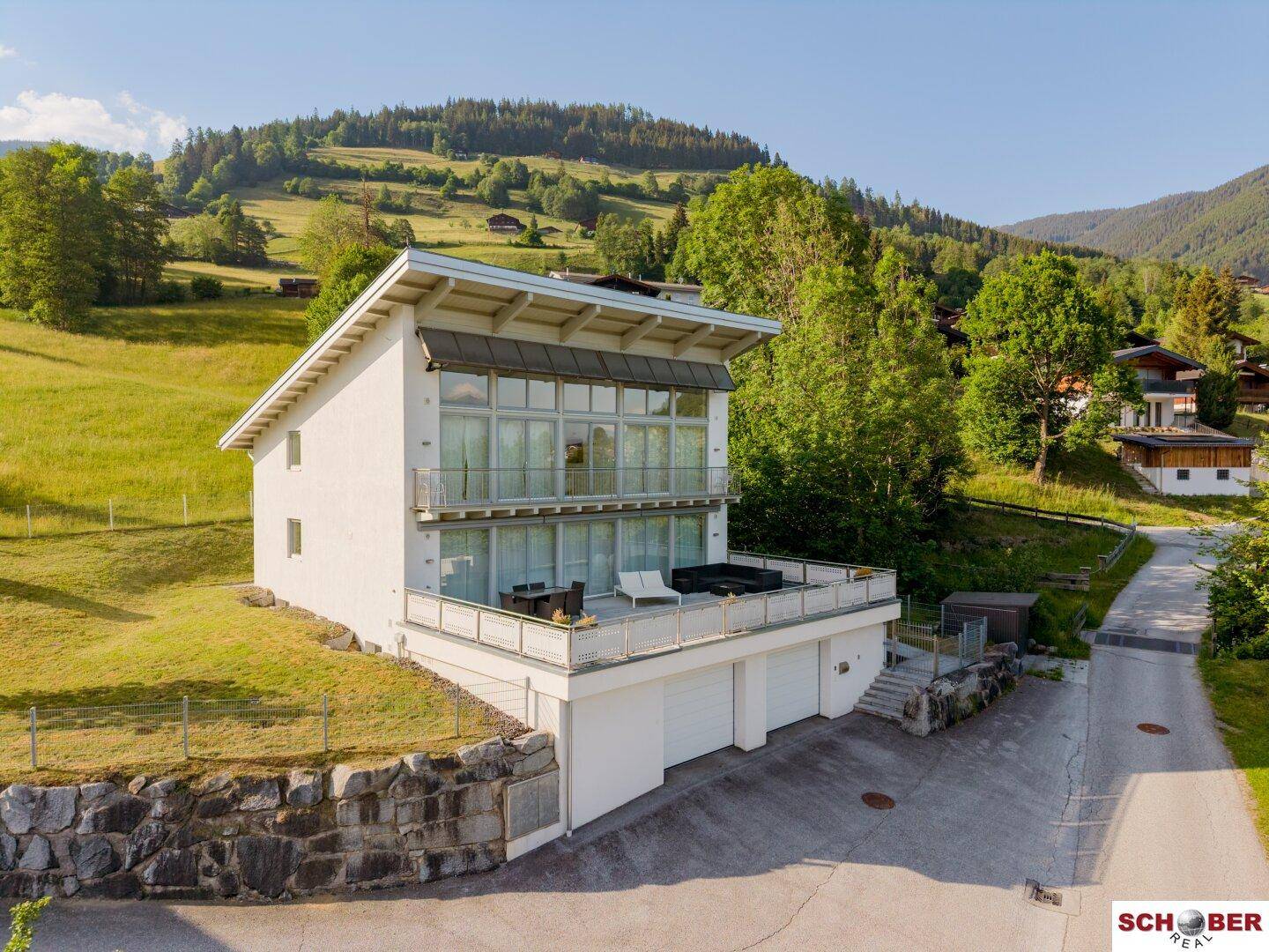 Helles, modernes Wohnhaus mit großen Glasfronten, Balkonen und einer sonnigen Terrasse mit Bergblick.