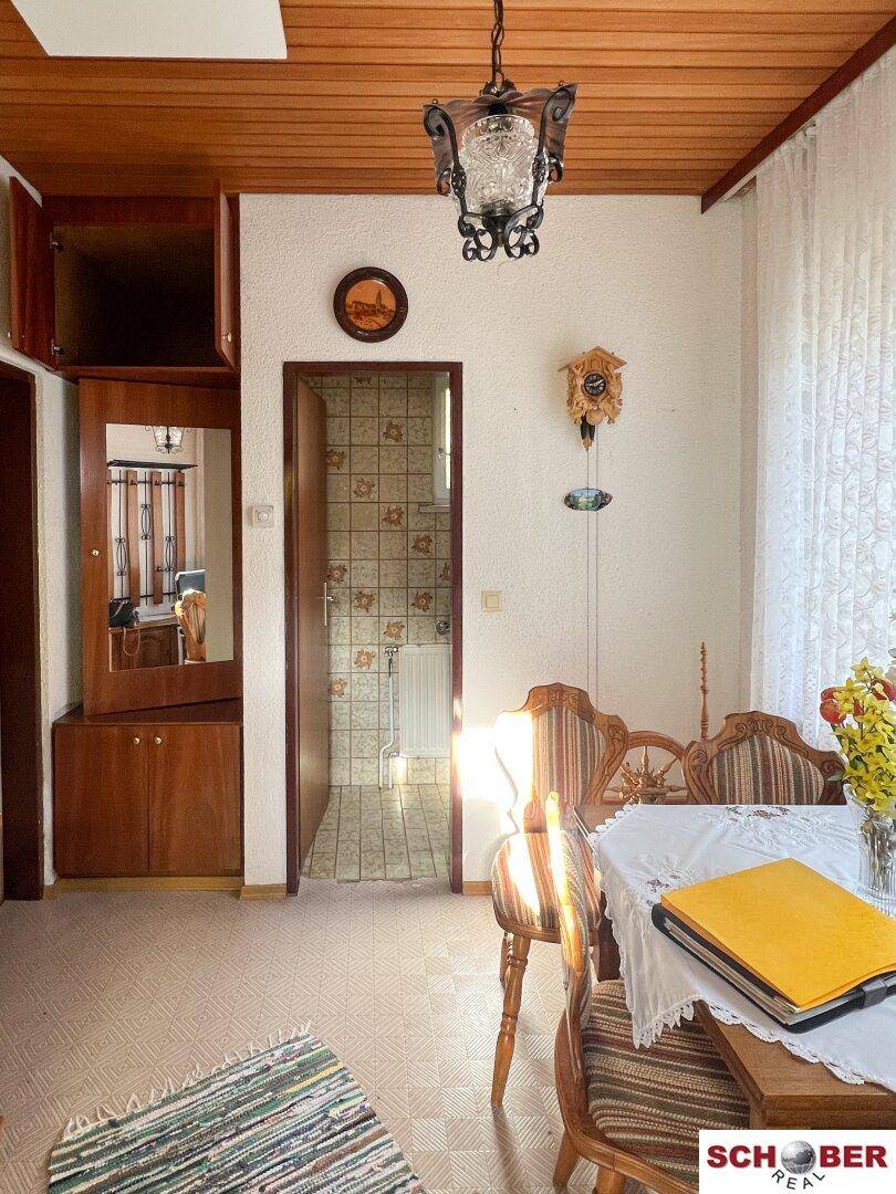 Traditioneller Essbereich mit Holzdecke und Blick in ein gefliestes Badezimmer.