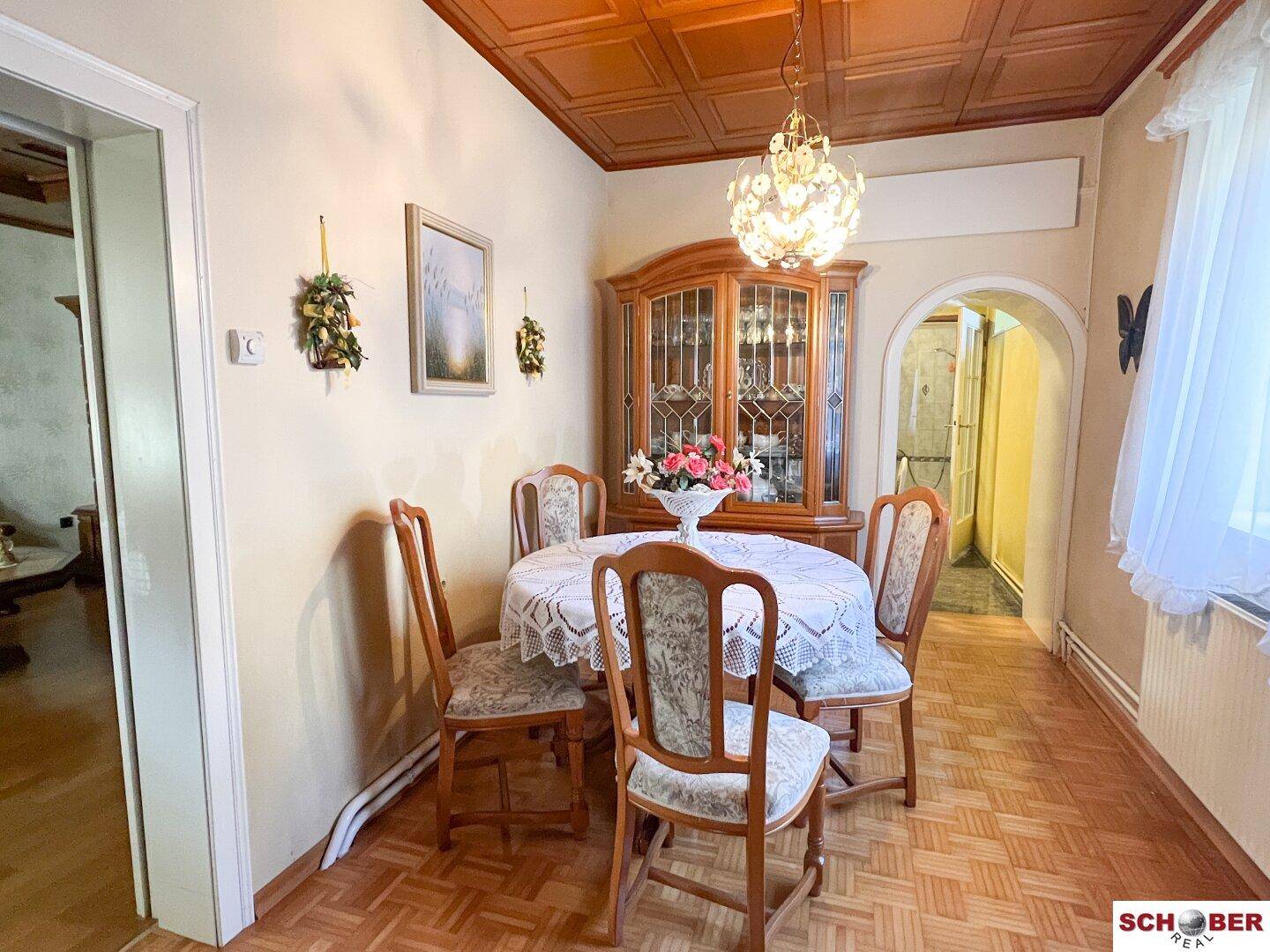 Gemütlicher Essbereich mit rundem Tisch, Holzparkett und einem antiken Vitrinenschrank.