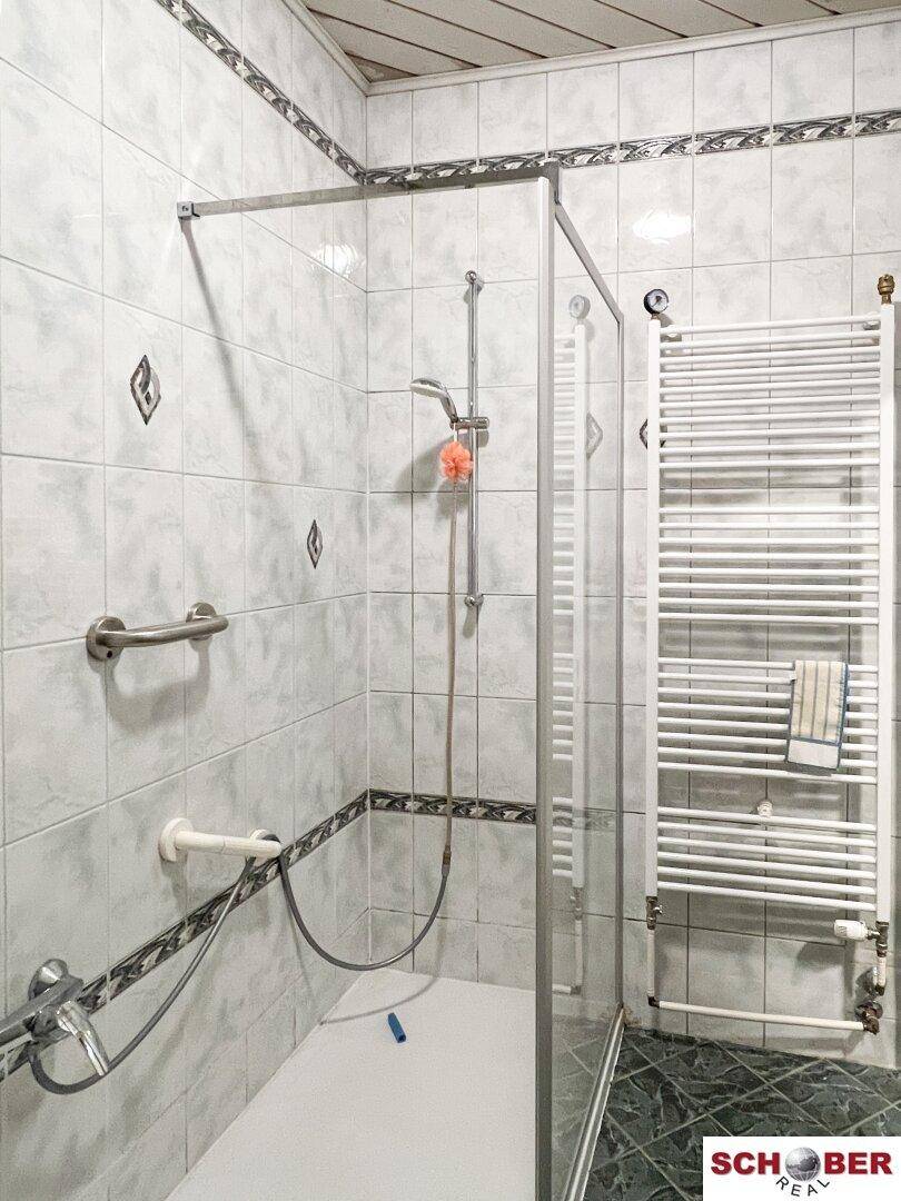 Badezimmer mit Duschkabine, weißen Fliesen und praktischem Handtuchheizkörper.