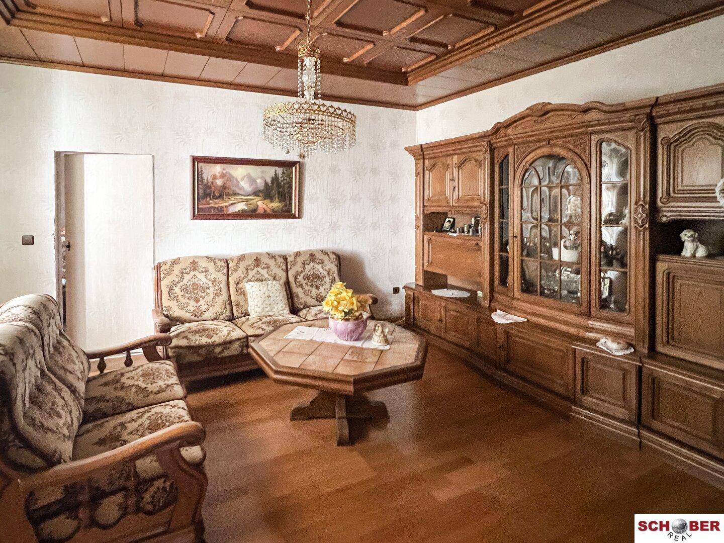 Geräumiges Wohnzimmer mit dunklen Holzmöbeln, Parkettboden und einem Kronleuchter.