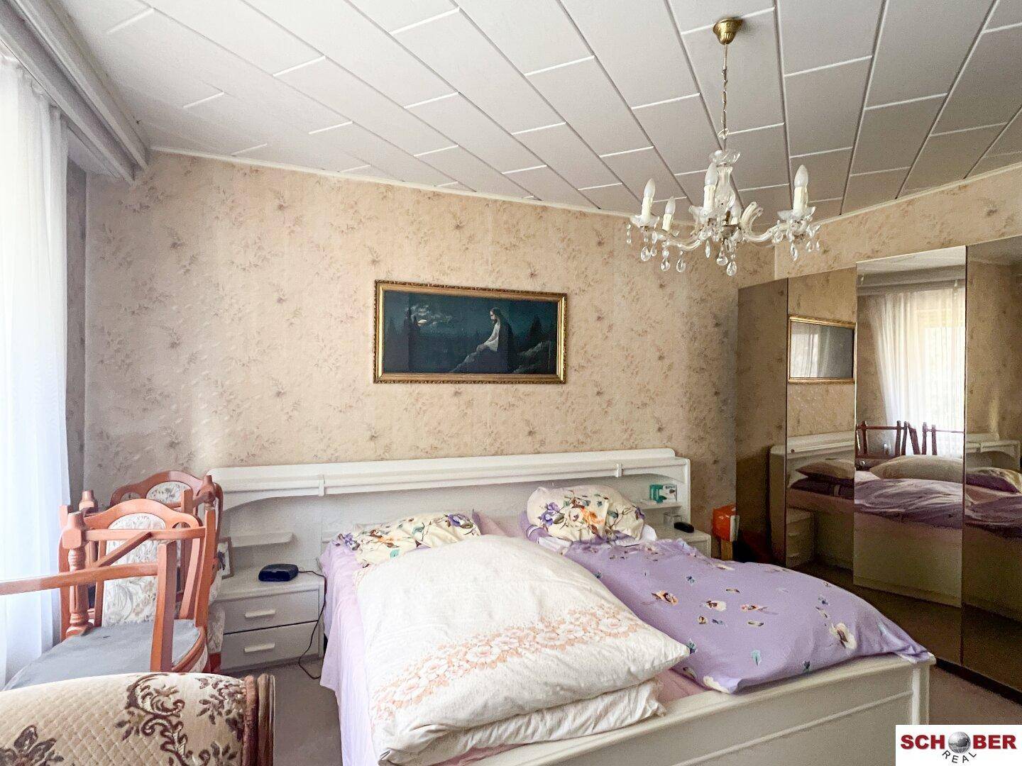 Schlafzimmer mit Doppelbett, Spiegelschrank und Kronleuchter, hell und geräumig.