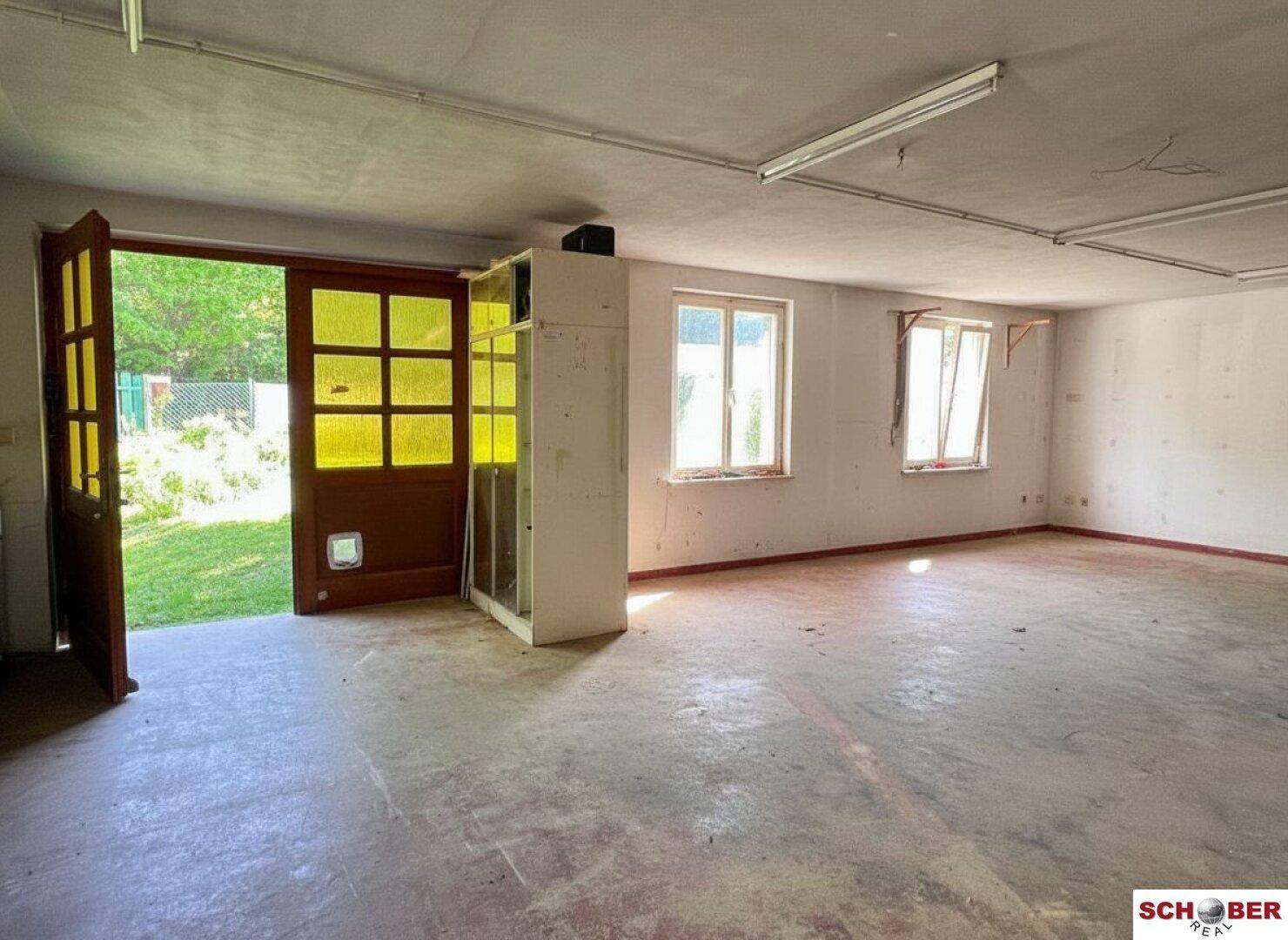Innenansicht einer großen Garage oder eines Abstellraums mit Fenstern und Betonboden.