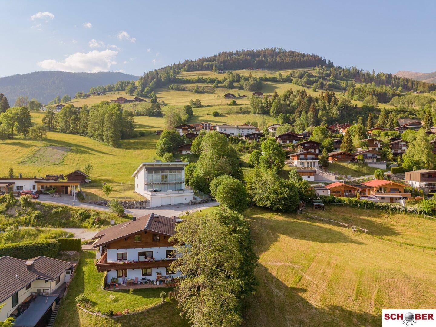 Luftaufnahme eines malerischen Dorfes in einer grünen Berglandschaft mit verschiedenen Wohnhäusern.