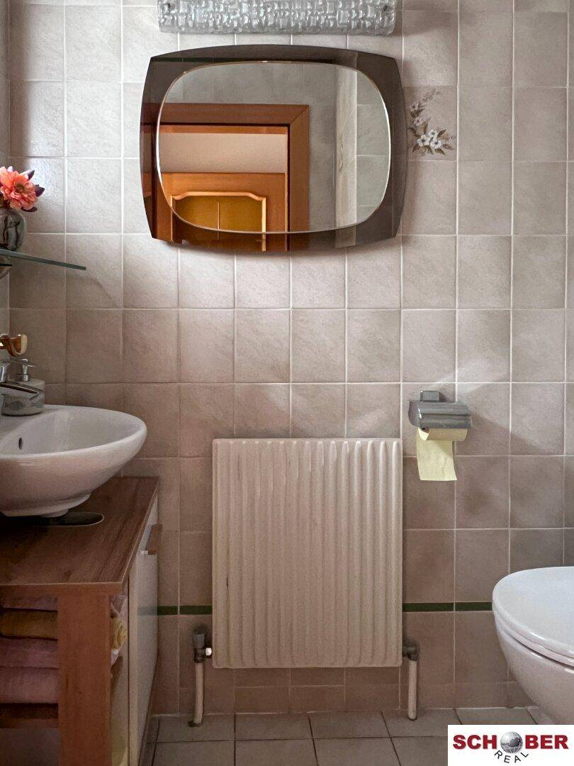 Kleines WC mit Waschbecken, Spiegel und Heizkörper, funktional und hell gefliest.