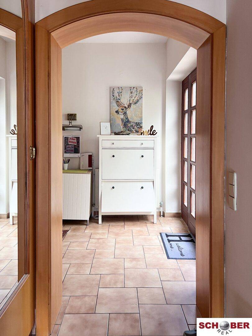 Heller Eingangsbereich mit Fliesenboden, Schuhschrank und Holztür mit Glaseinsätzen.