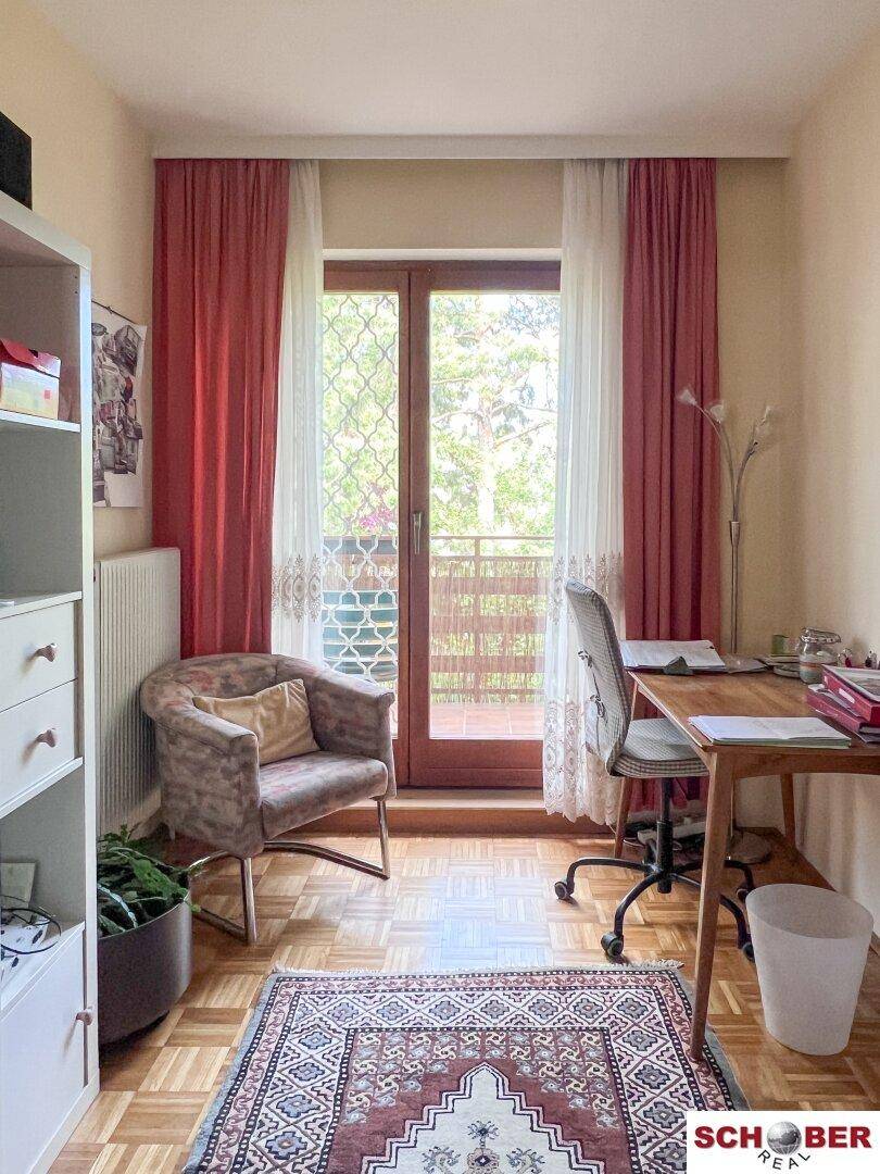Helles Arbeitszimmer mit Parkettboden, Schreibtisch und Zugang zum Balkon.