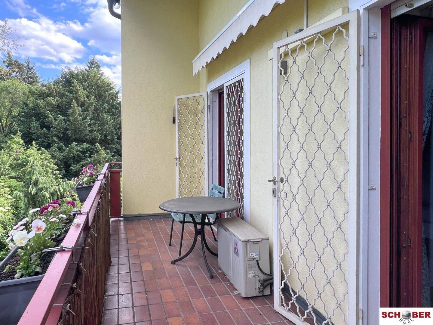 Gemütlicher Balkon mit Fliesenboden, kleinem Tisch und Blick auf die umliegenden Bäume.
