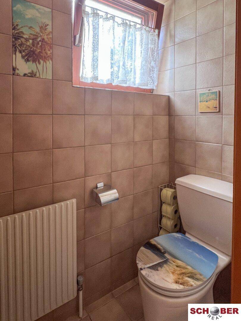 Kleines WC mit Fliesenboden, Toilette und Fenster, einfach und funktional gestaltet.
