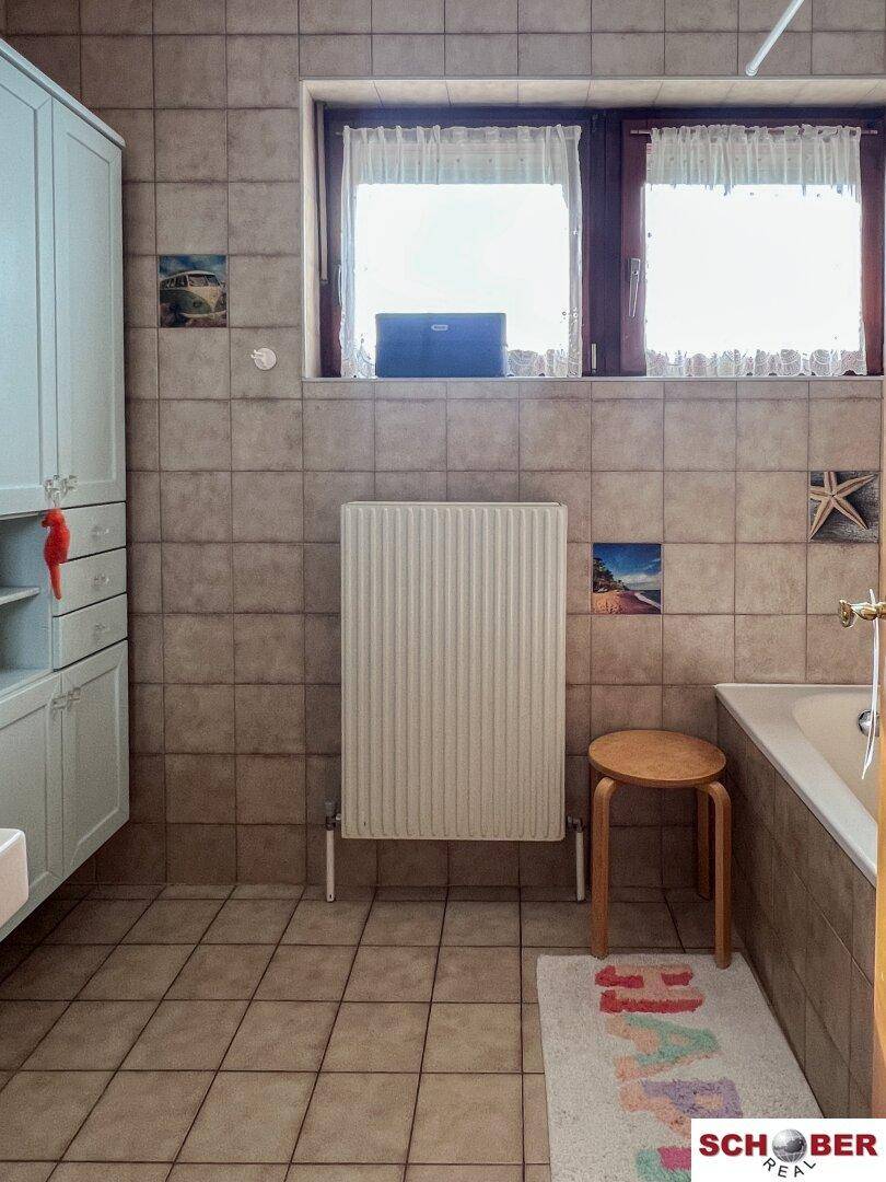 Badezimmer mit Fliesenboden, Badewanne, Waschbecken und Fenster für Tageslicht.