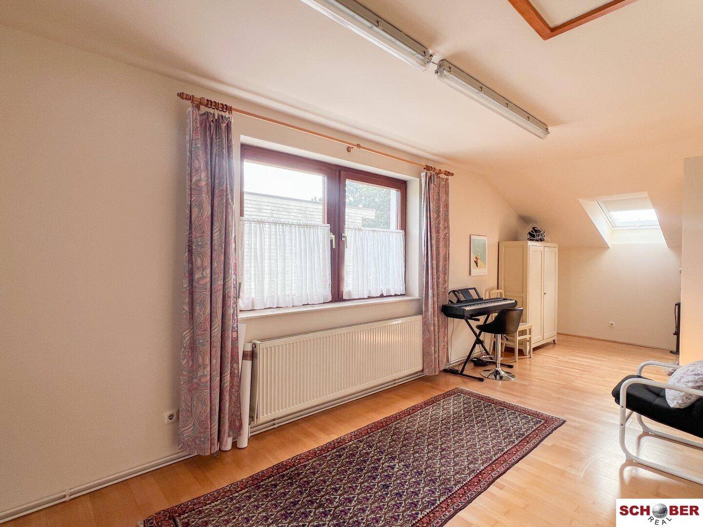 Helles Dachzimmer mit Holzboden, großem Fenster und schrägen Wänden.