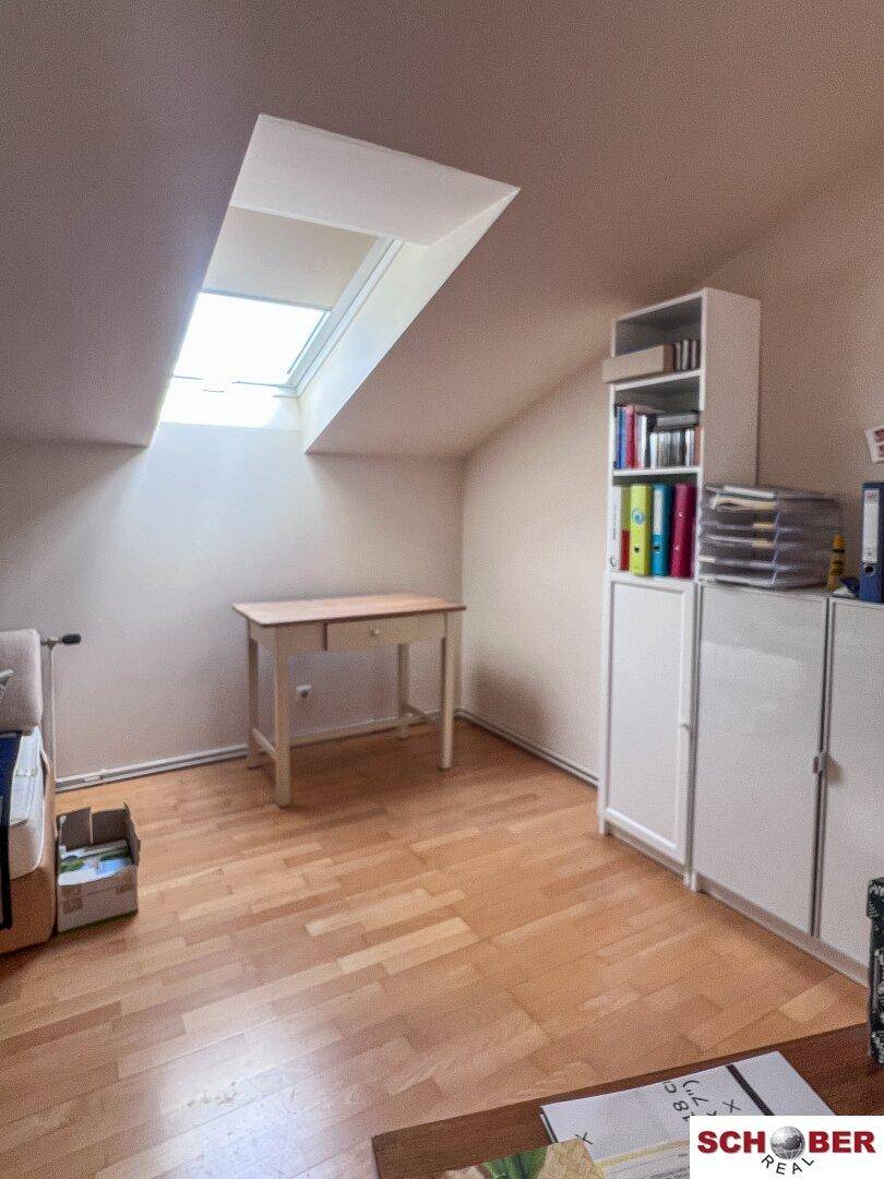 Dachzimmer mit Holzboden, Schreibtisch und Dachfenster, ideal als Arbeits- oder Gästezimmer.