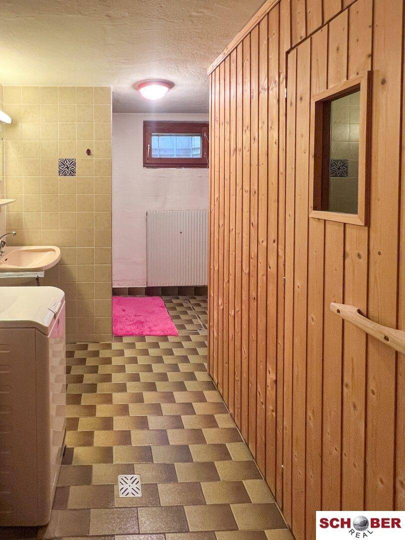 Kellerbad mit Fliesenboden, Waschbecken und angrenzender Holzsauna.