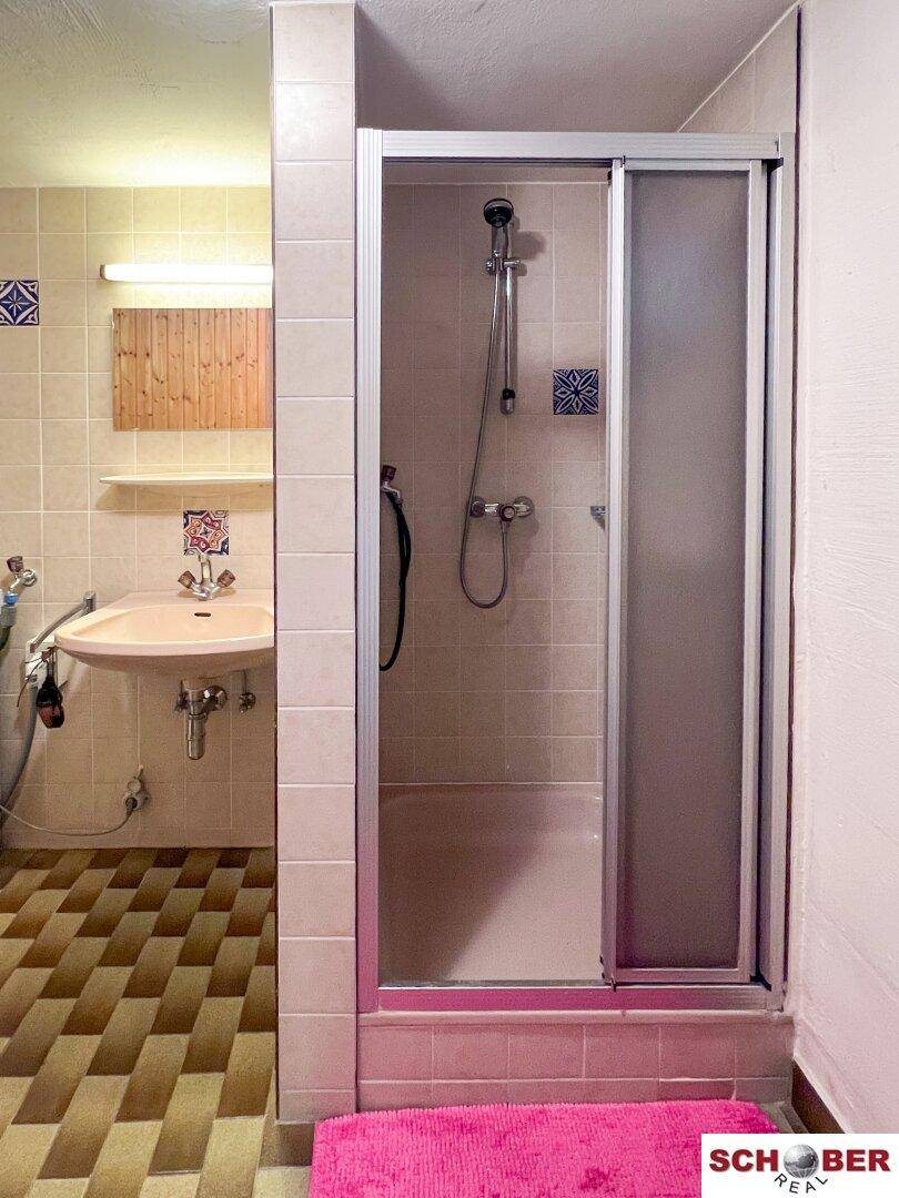 Kellerbad mit Duschkabine, Waschbecken und Fliesenboden, funktional und hell.