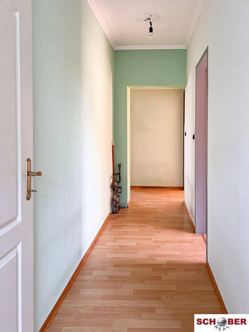 Langer Flur mit hellem Laminatboden und Wänden in Pastellgrün, der zu weiteren Räumen führt.