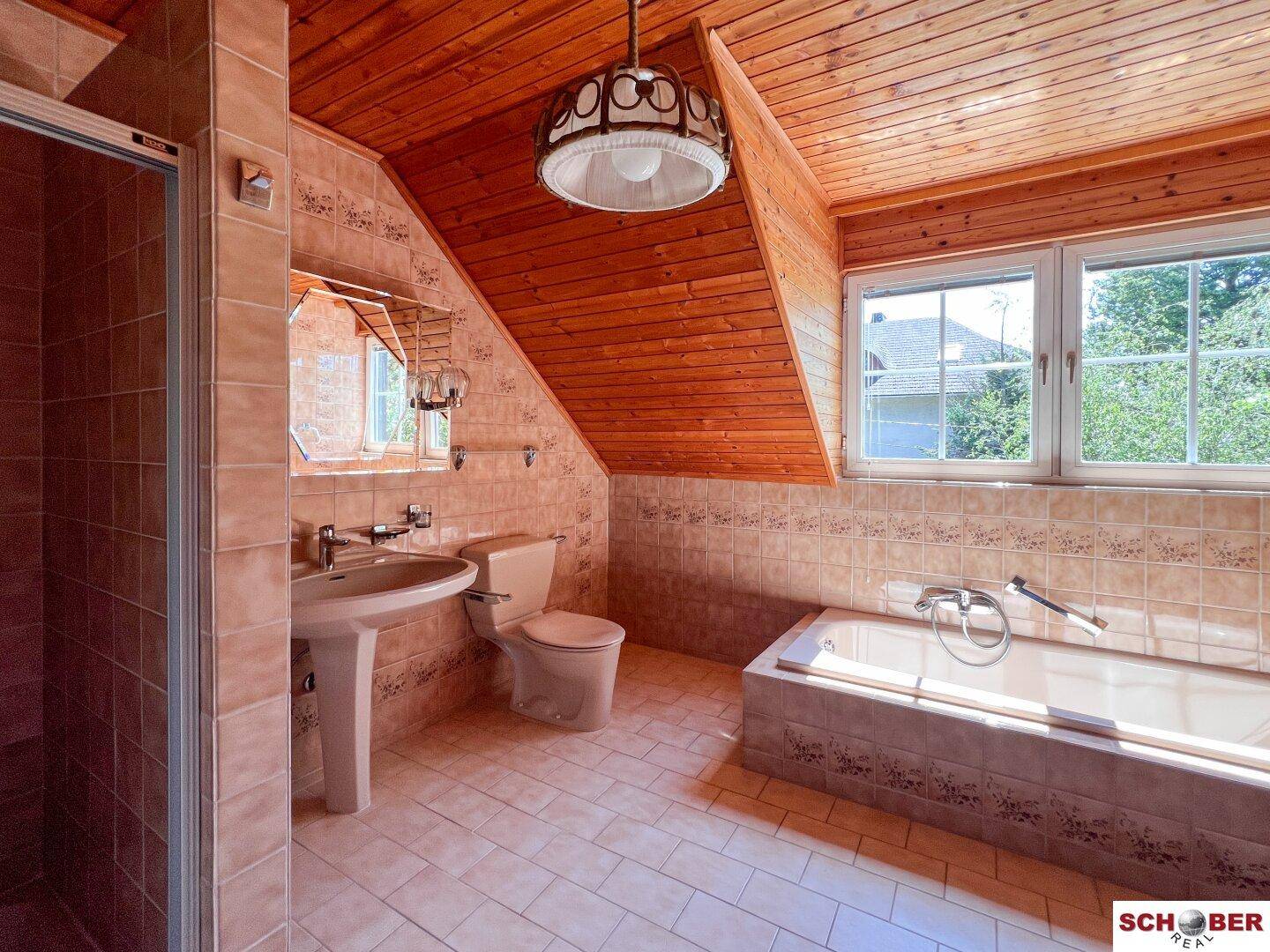 Badezimmer im Dachgeschoss mit Badewanne, Waschbecken und Holzverkleidung an der Decke und Wänden.