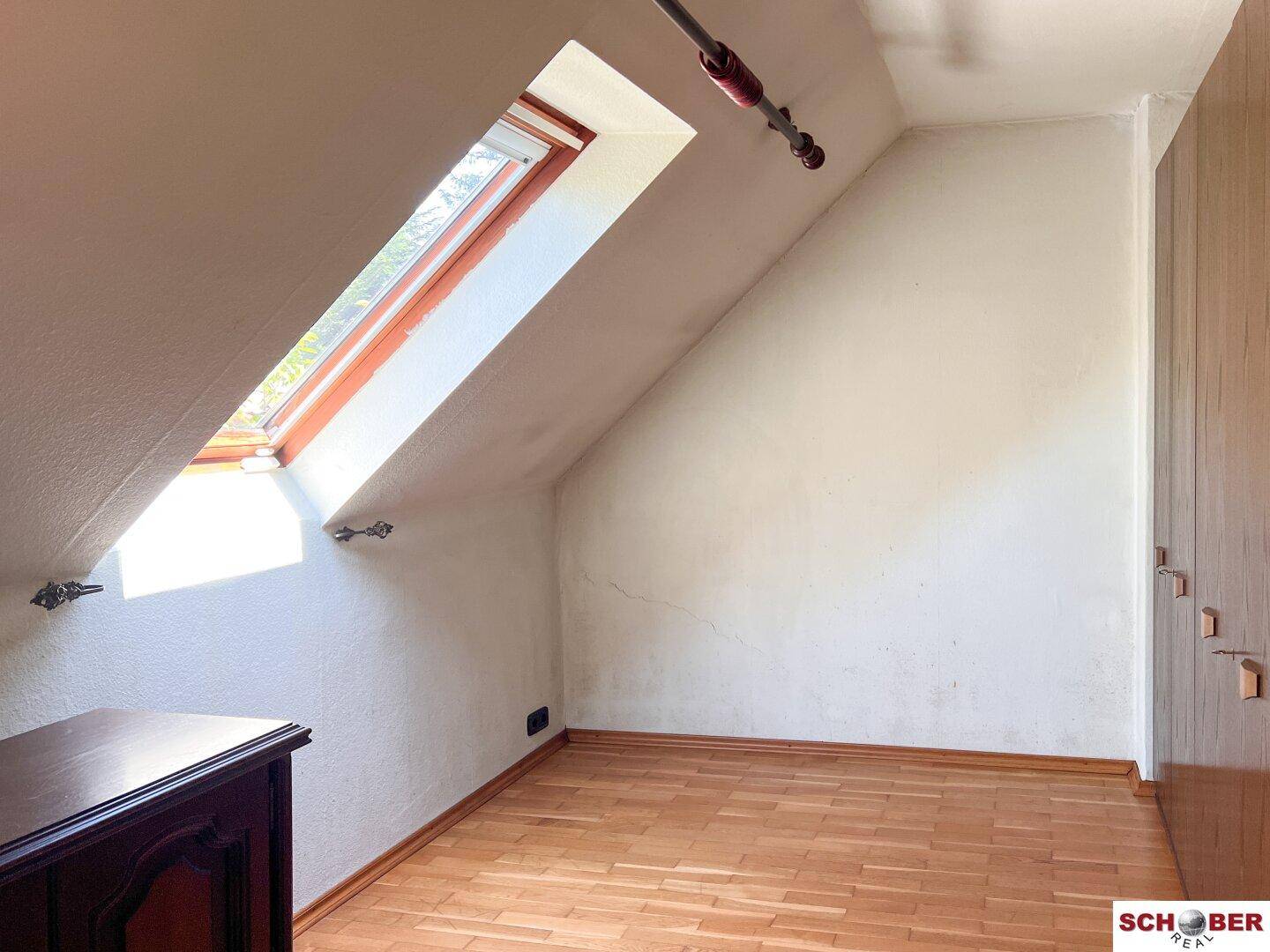 Helles Dachzimmer mit Holzboden, Dachfenster und schrägen Wänden, ideal als Schlaf- oder Arbeitszimmer.