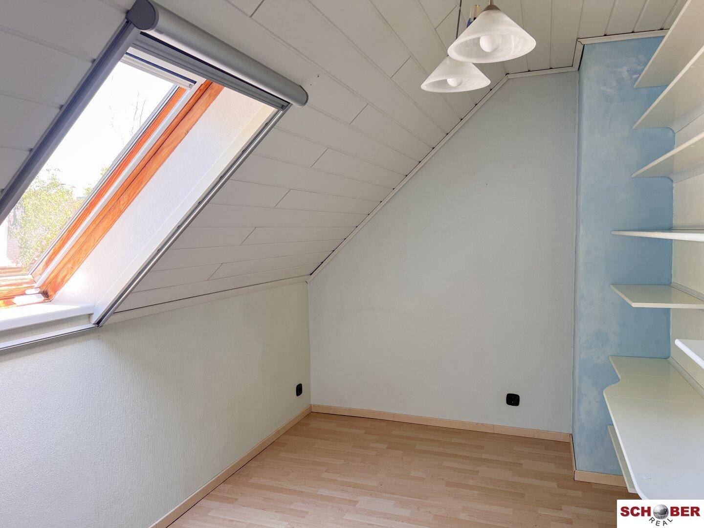 Helles Dachzimmer mit Dachfenster, Holzdecke und eingebauten Regalen, bietet zusätzlichen Stauraum.