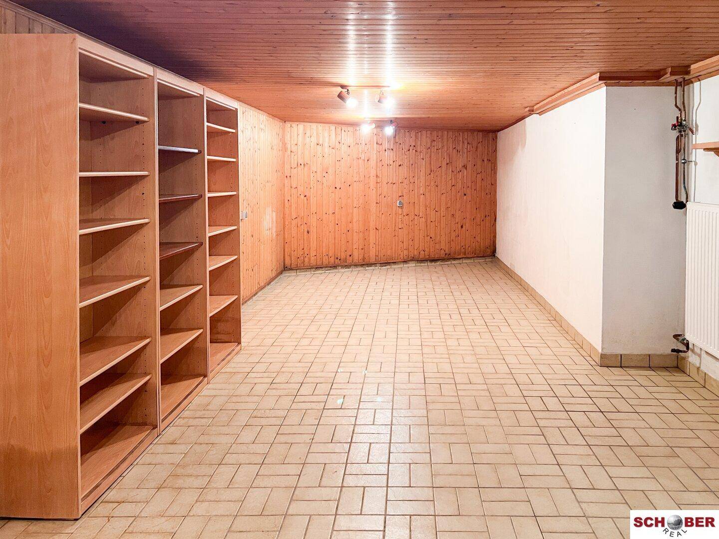Geräumiger Kellerraum mit Holzverkleidung, Fliesenboden und Regalen, ideal als Lagerfläche.