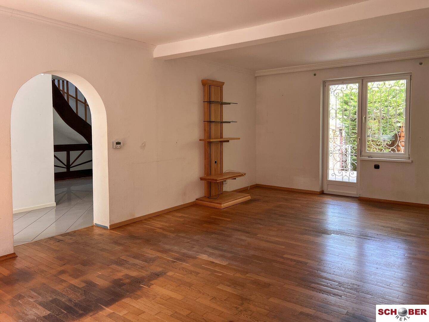 Geräumiges Wohnzimmer mit Holzboden und dekorativem Regal, offen zum Treppenbereich und hellen Fenstern.