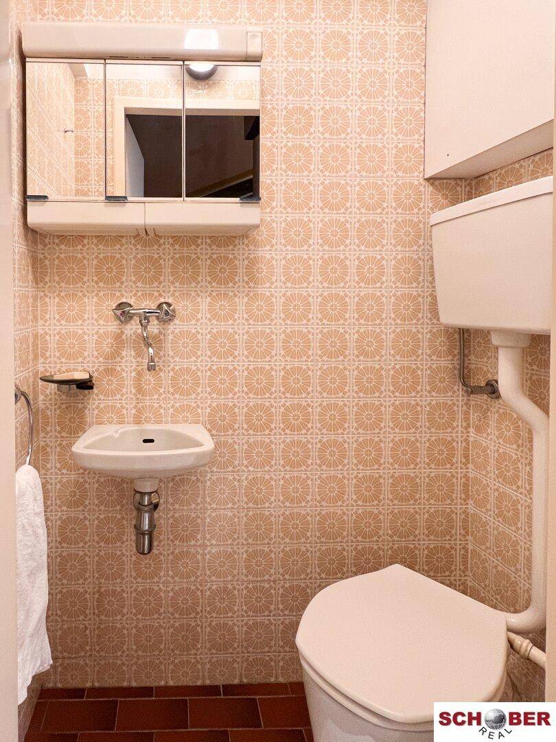 Kleines Badezimmer oder Gäste-WC mit Toilette und Waschbecken, verziert mit gemusterten Fliesen.