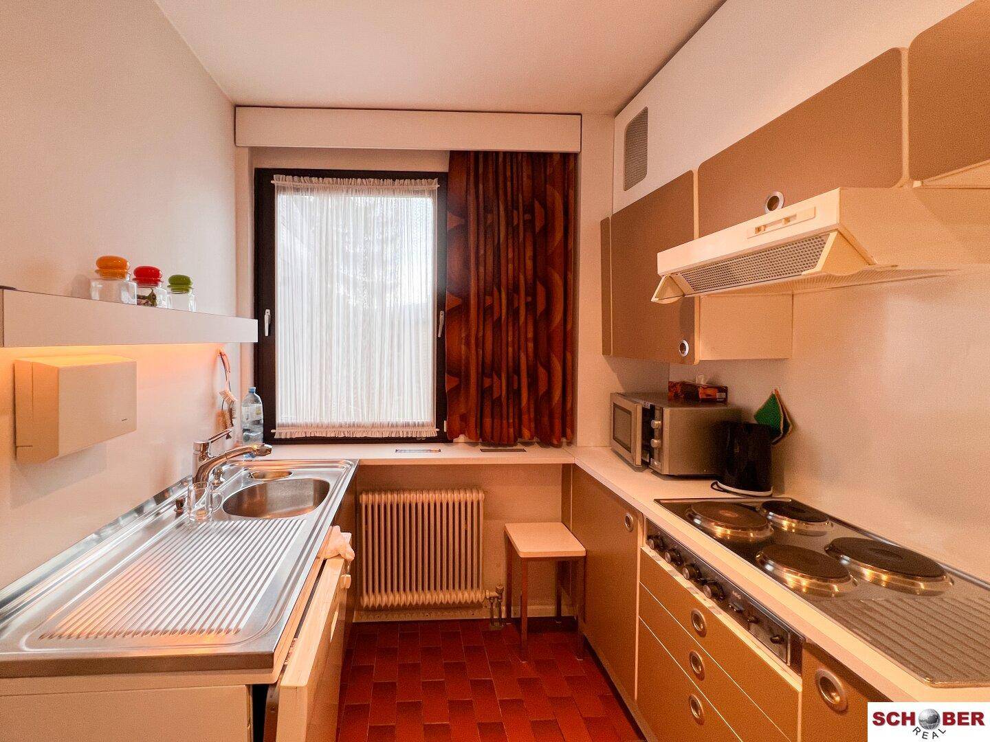 Praktische Küche mit Spüle, Herd und Mikrowelle, ausgestattet mit braunen Schränken und einem Fenster.