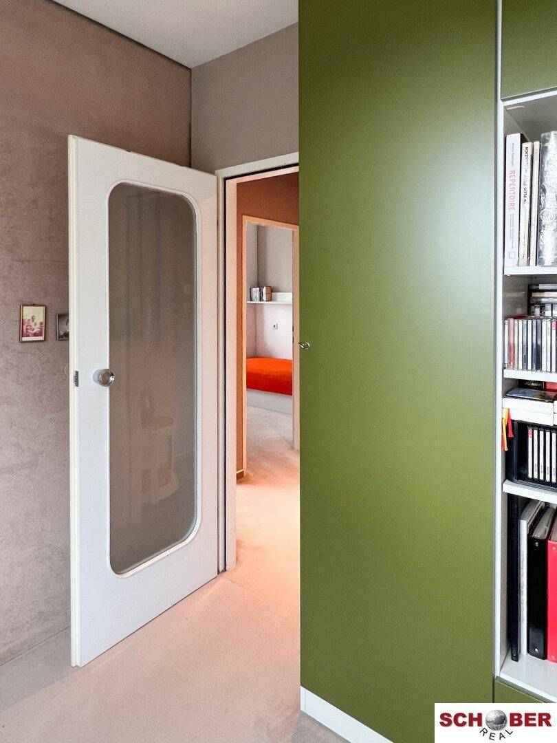 Flur oder Übergangsbereich mit einer weißen Tür und einem integrierten grünen Bücherregal.